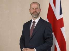 Jonathan Reynolds, Business Secretary, in a dark suit and red tie standing beside a Union Flag