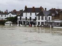 Floodwater from the River Thames lapping at the front of the Swan Hotel and neighbouring riverside buildings in Staines-upon-Thames under a grey sky
