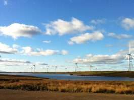Wind turbines at Whitelee Wind Farm in East Renfrewshire across a loch under a blue sky, file photograph